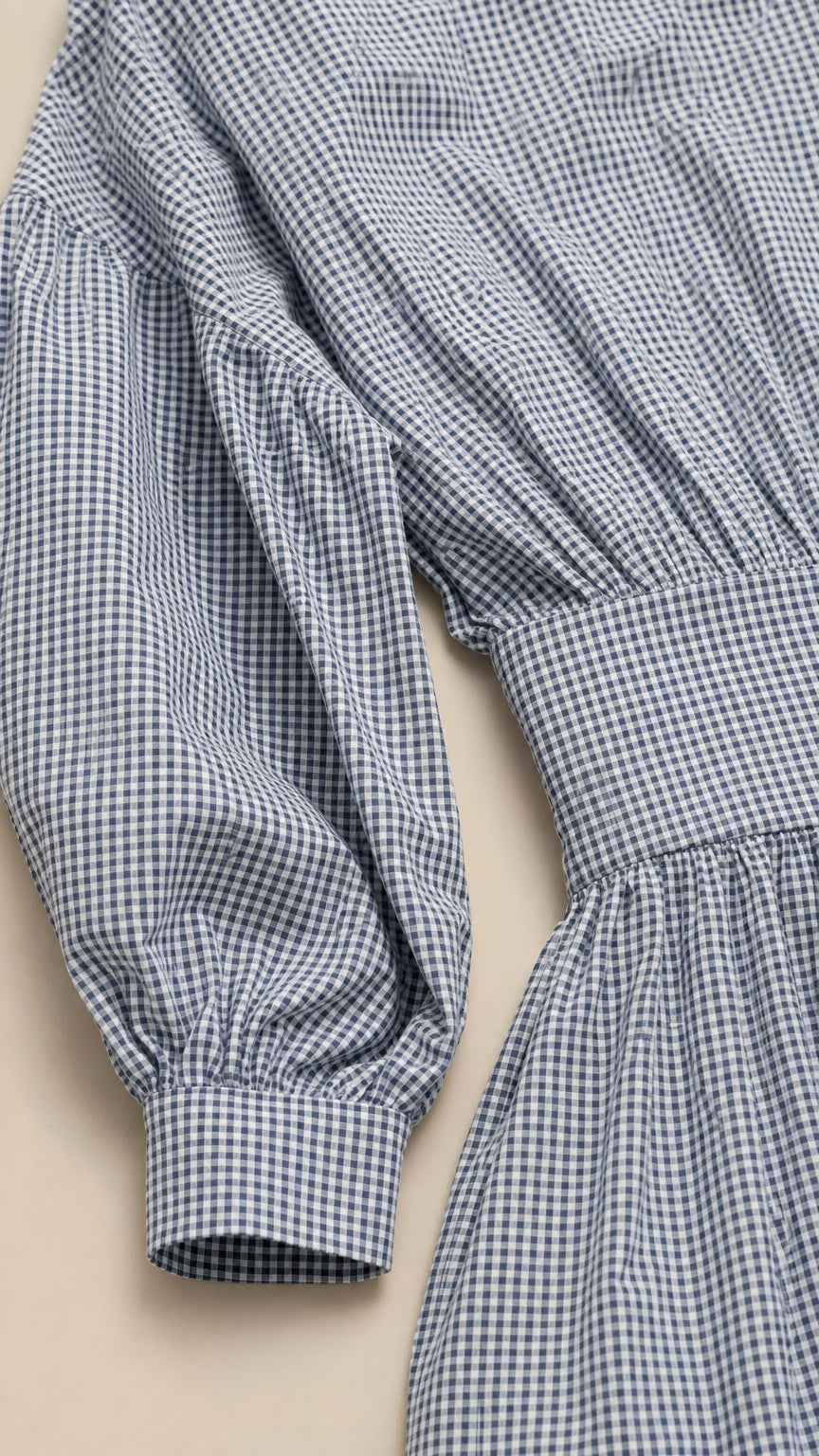 Close-up detail of blue gingham fabric, sleeve, and waistband