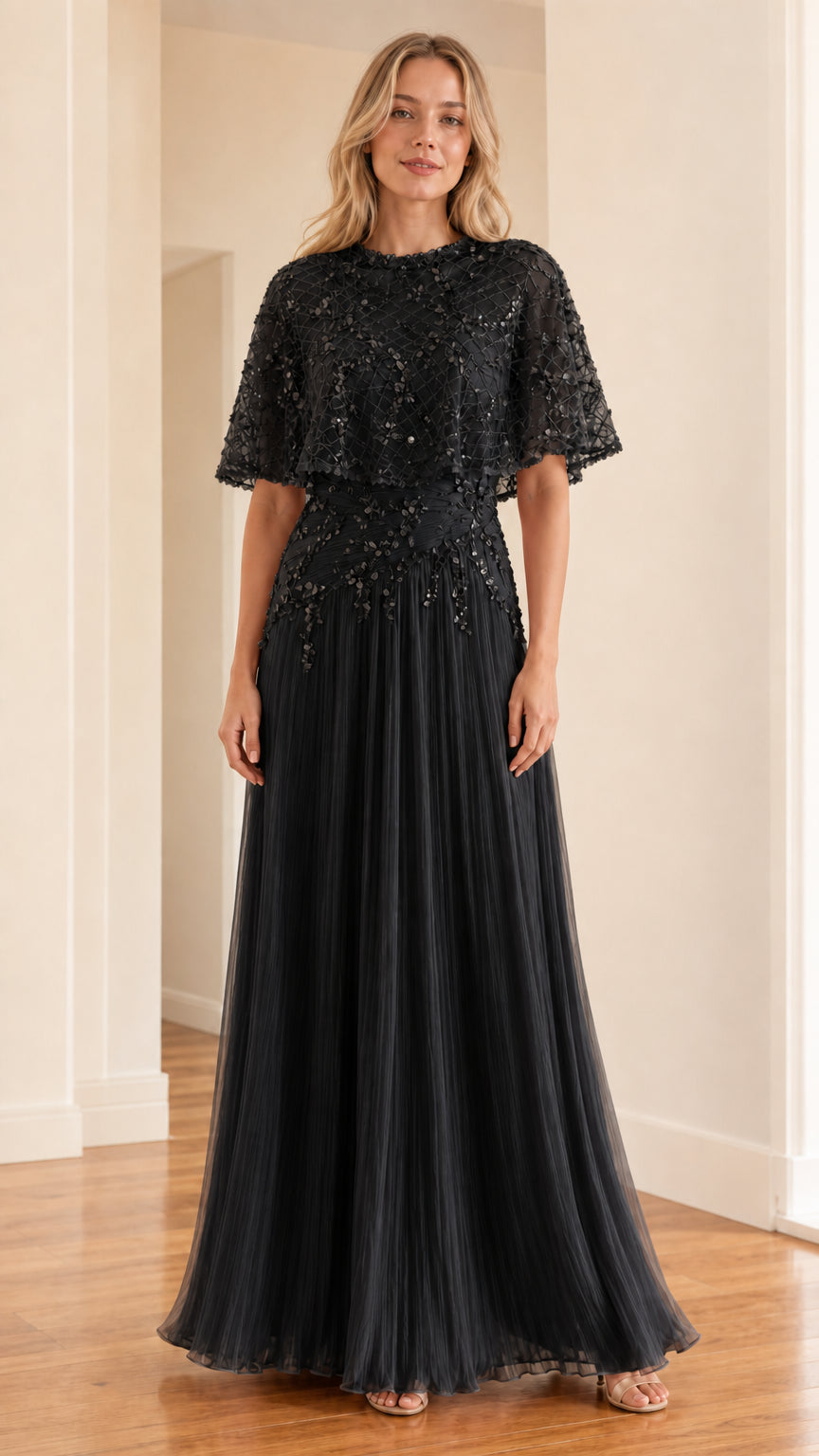 Front view of black evening dress with cape overlay and pleated skirt
